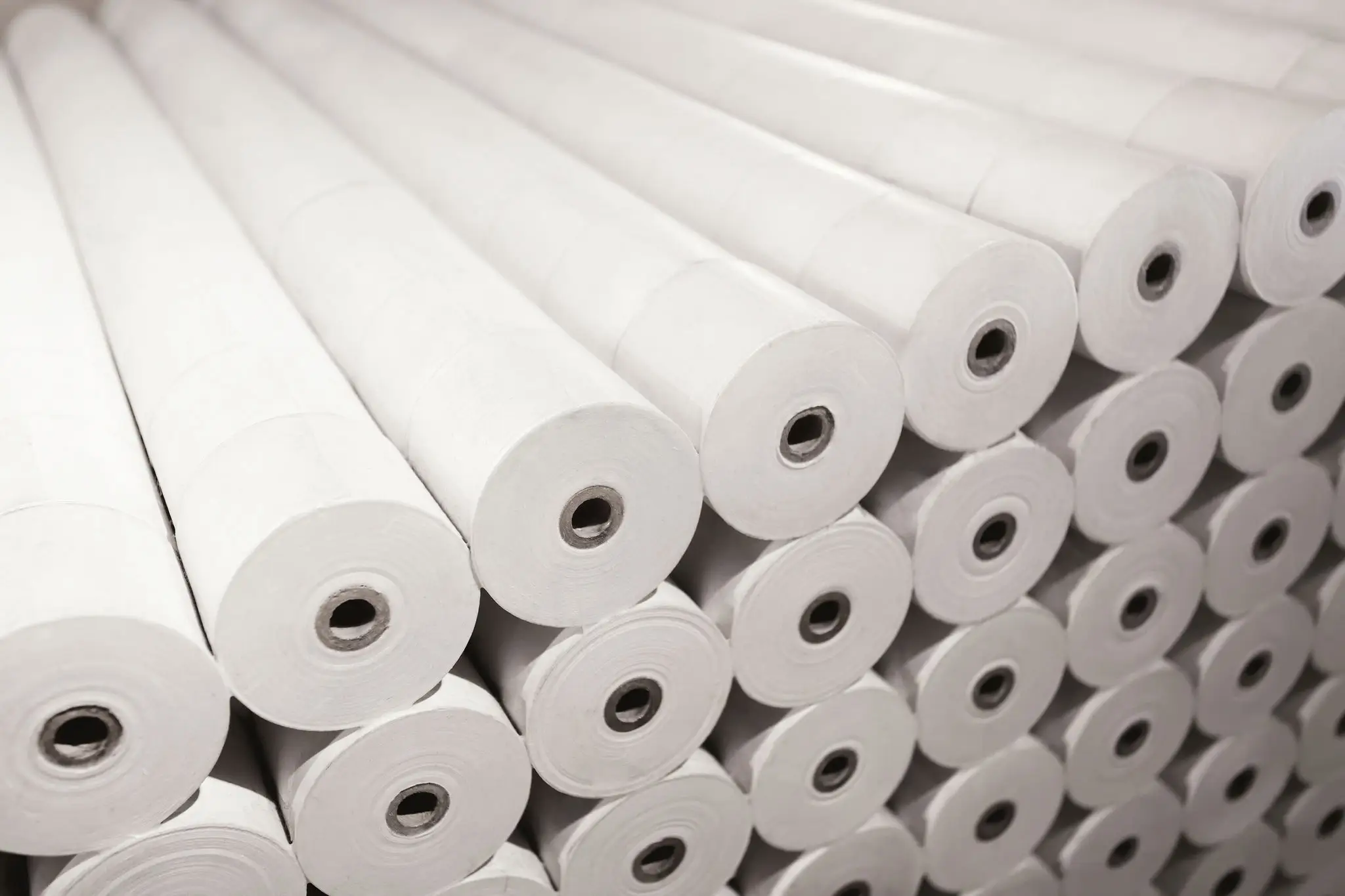 Stacked rolls of white paper in warehouse.